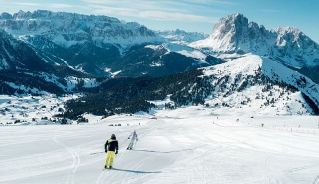 Skiers on a snowy mountain slope with rugged peaks in the background